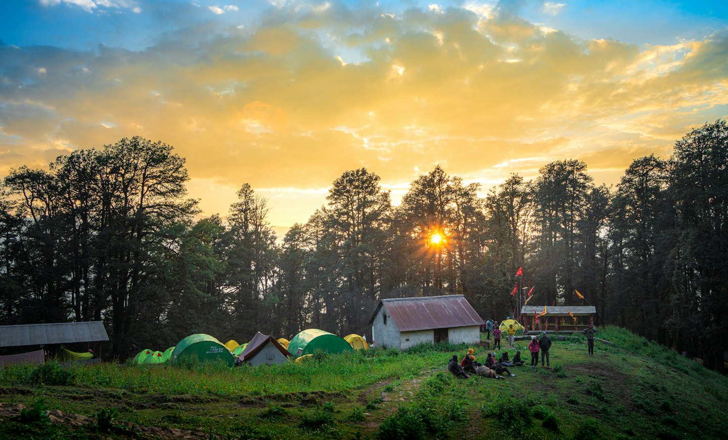 Campers relax by tents on a grassy hill at sunset.