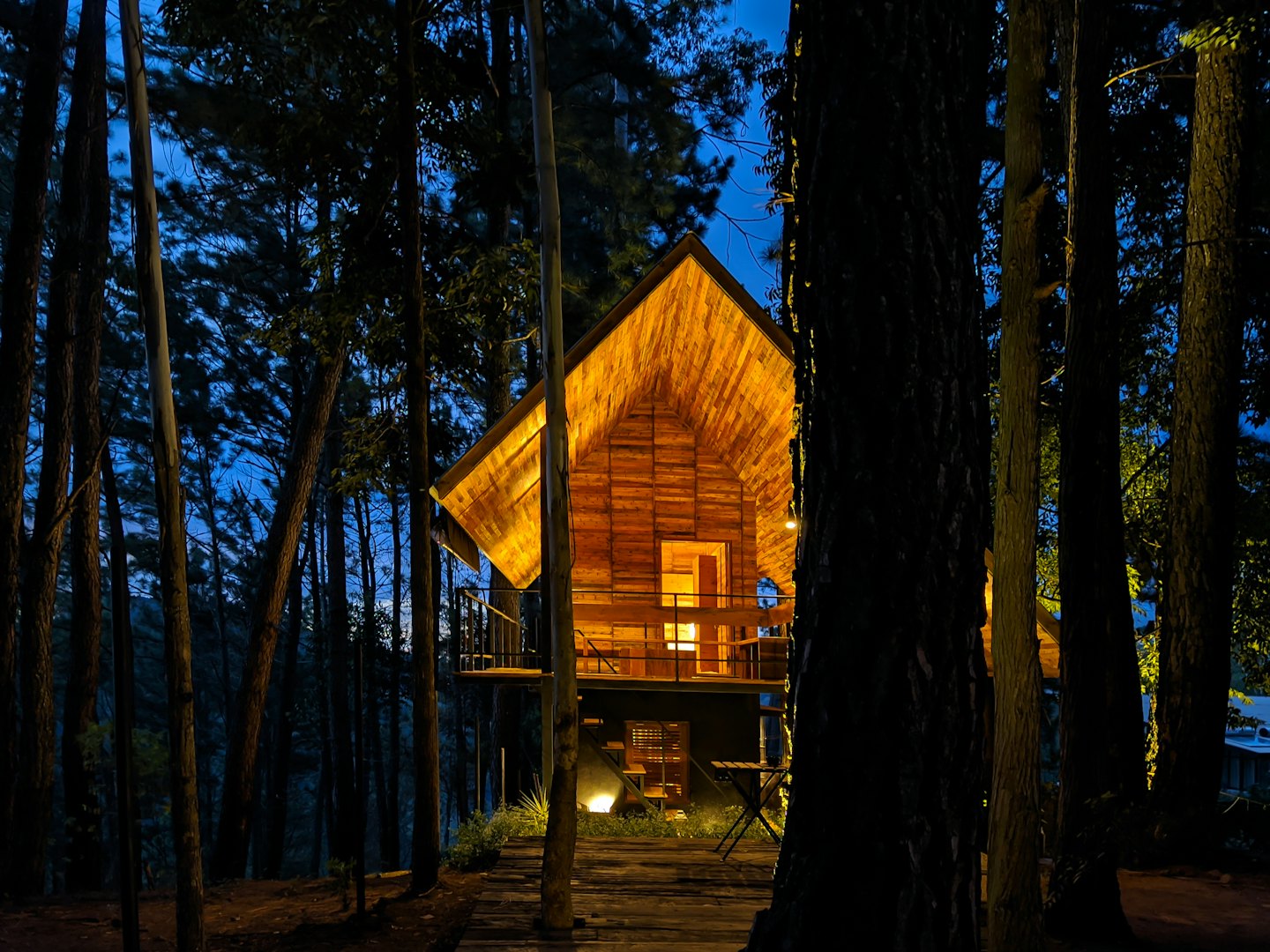 Cozy wooden cabin lit up at dusk surrounded by pine trees.
